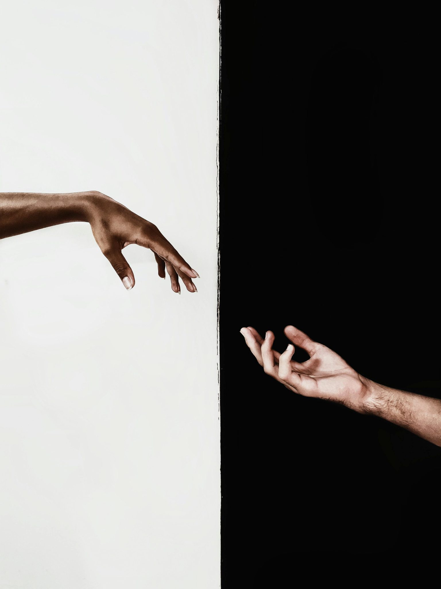 Two hands reaching across a stark black and white divide, symbolizing connection and unity.